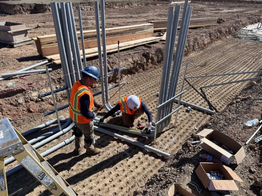 Two workmen installing upright electrical conduit